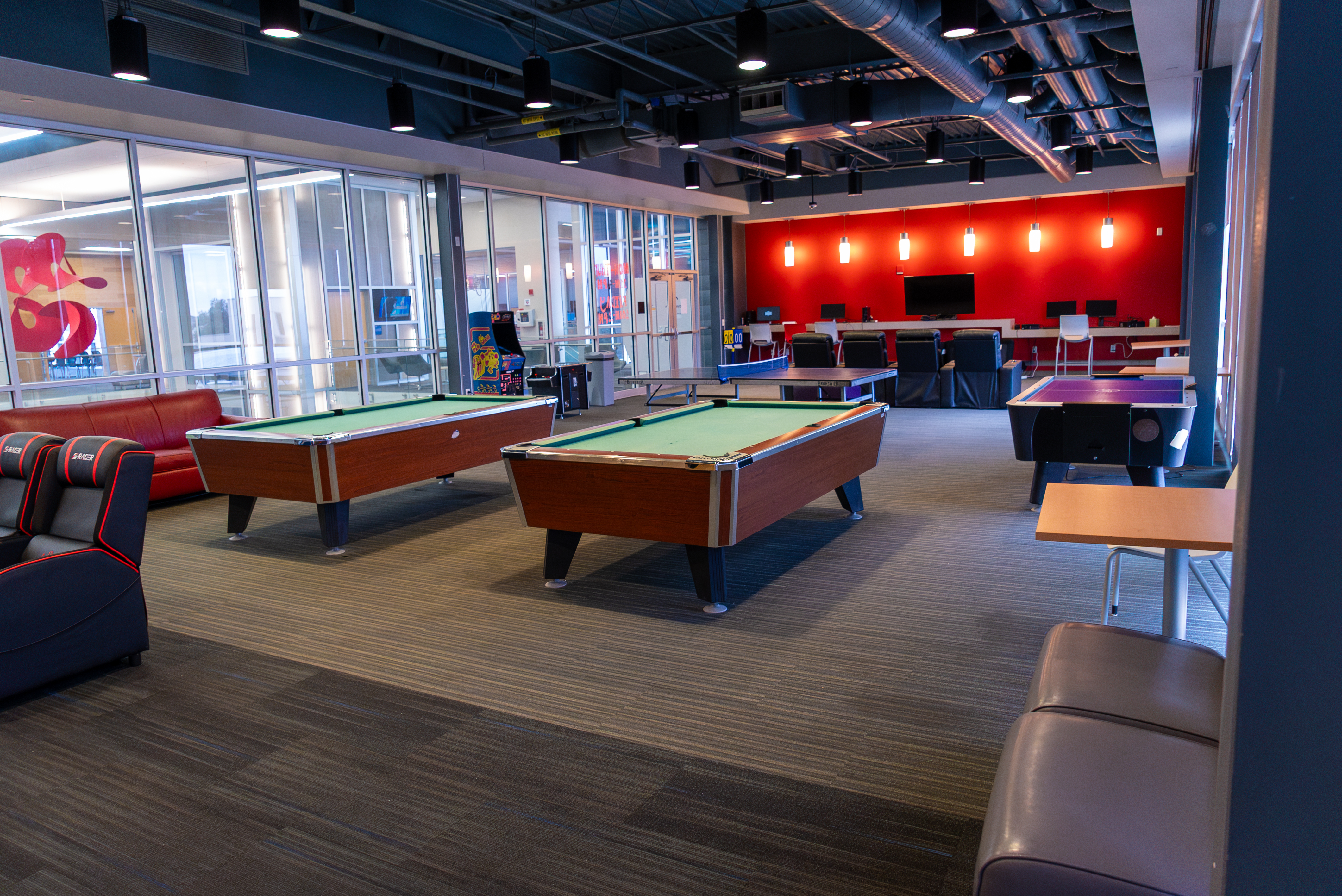 A shot of the empty game room filled with chairs, two pool tables, an air hockey table and stations for video games.