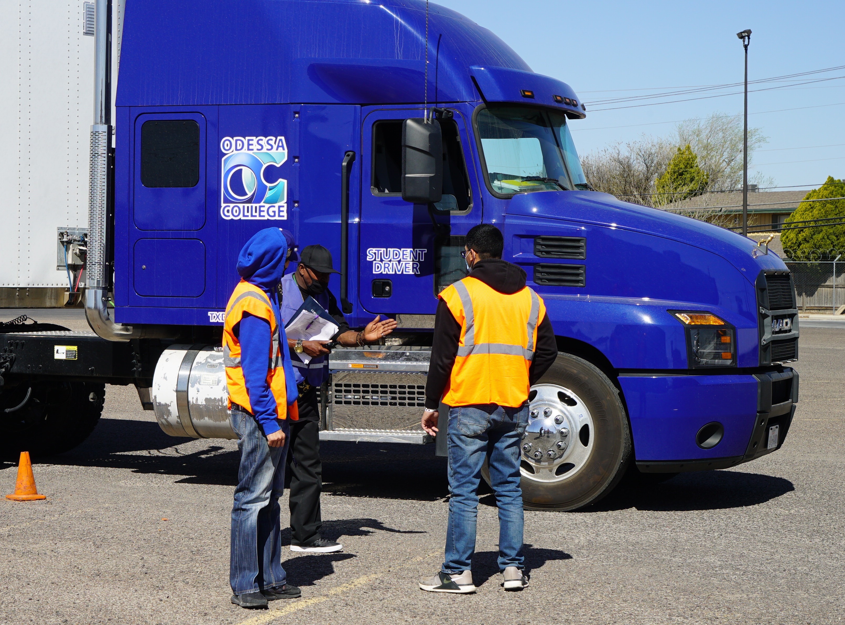 Two students with a professor in front of a trailer with the OC logo